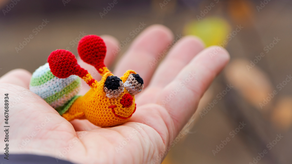 Textile handmade funny happy snail toy in hand on natural blurry background. macro photo. multi-colored snail. beautiful toy, close-up. the concept of childhood, games, education Textile handmade funny happy snail toy in hand on natural blurry background. macro photo. multi-colored snail. beautiful toy, close-up. the concept of childhood, games, education