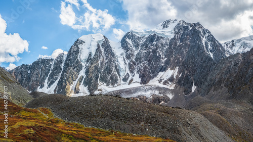 Atmospheric alpine landscape with massive hanging glacier on snowy mountain peak. Big balcony serac on glacial edge. Blue cloudy sky over snowbound mountains. Majestic scenery on high altitude.