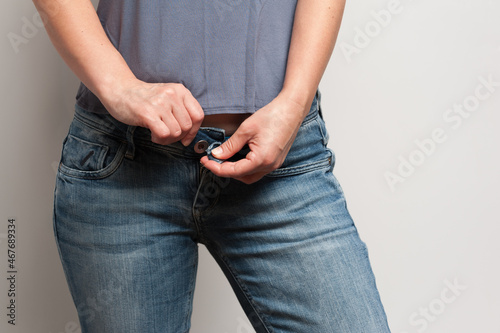 A woman trying on jeans fastening a button and zipper