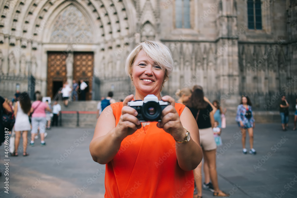 Positive adult woman standing near old cathedral and taking photos on camera