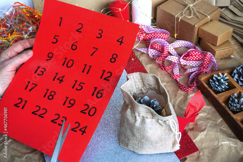 Women's hands cut the numbers for the advent calendar, on the table there are gift packages and a ready-made gift in a canvas bag, cones, ribbons. Preparing for Christmas. DIY