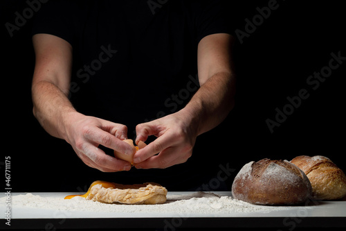 Cooking the bread. The chef's hands add a chicken egg that flies onto the white table with the flour and dough. Chef sprinkles white flour dust with a man's hand on a black background. Space for text.