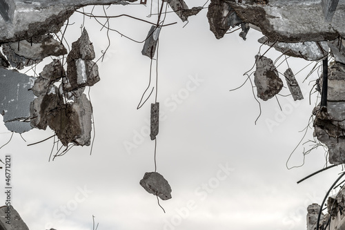 Concrete fragments hang on metal fittings against a gray sky. Background