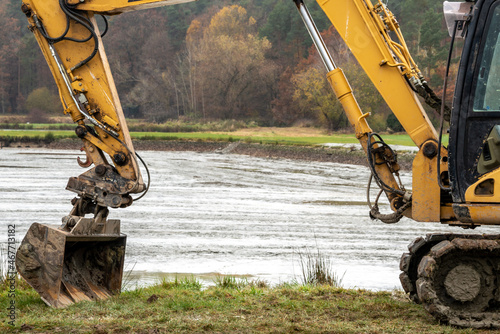 A yellow excavator in front of a muddy pond