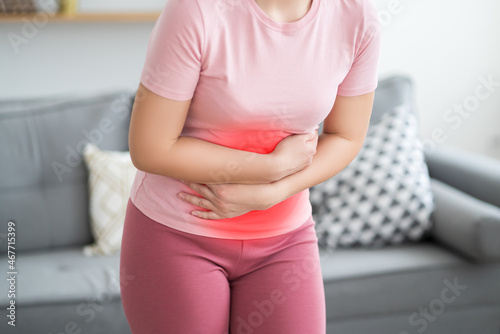 Stomach ache, symptoms of gastritis or pancreatitis, woman with abdominal pain at home interior photo
