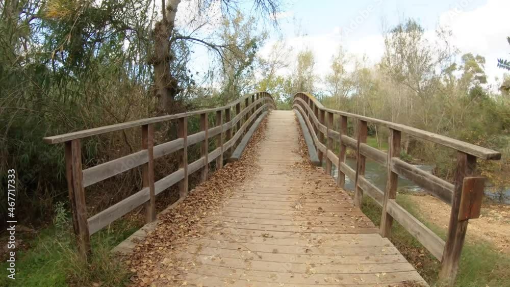 Wooden bridge over river in parkland. Hiking in park, going over river on wooden bridge, first person view Wooden bridge over river in parkland. Hiking in park, going over river on wooden bridge, first person view