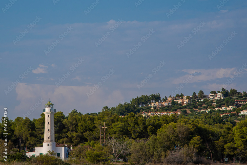 Possidi Lighthouse, Near Possidi cape (Ακρωτήριο Ποσείδι) lighthouse, built in 1864. Forest and houses in background. Chalkidiki on the Kasandra, Greece.
