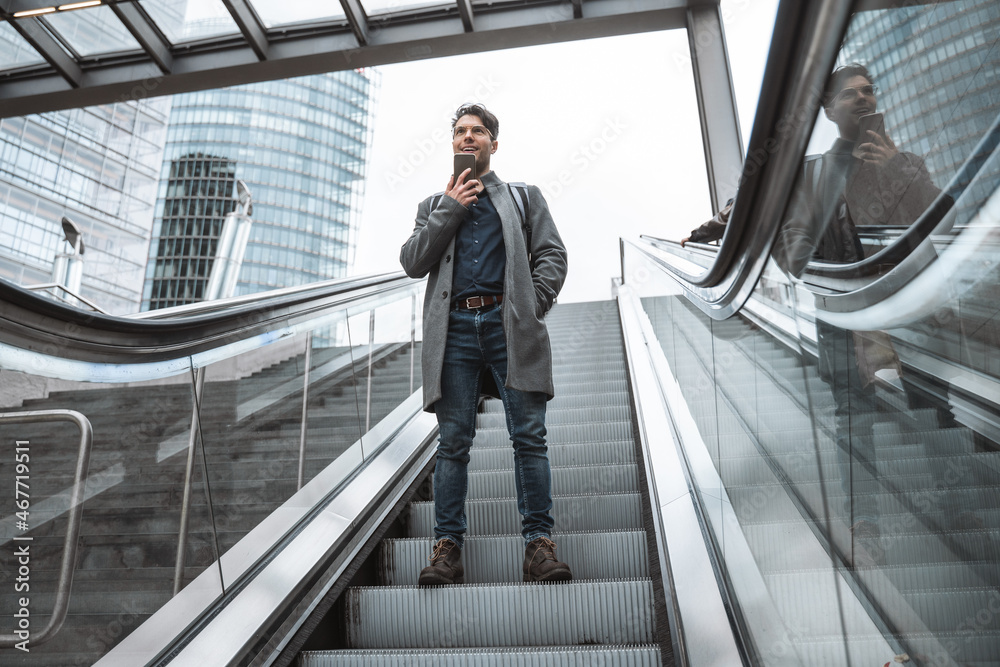 Businessman standing at the escalator with mobile phone and sending voice message Businessman standing at the escalator with mobile phone and sending voice message