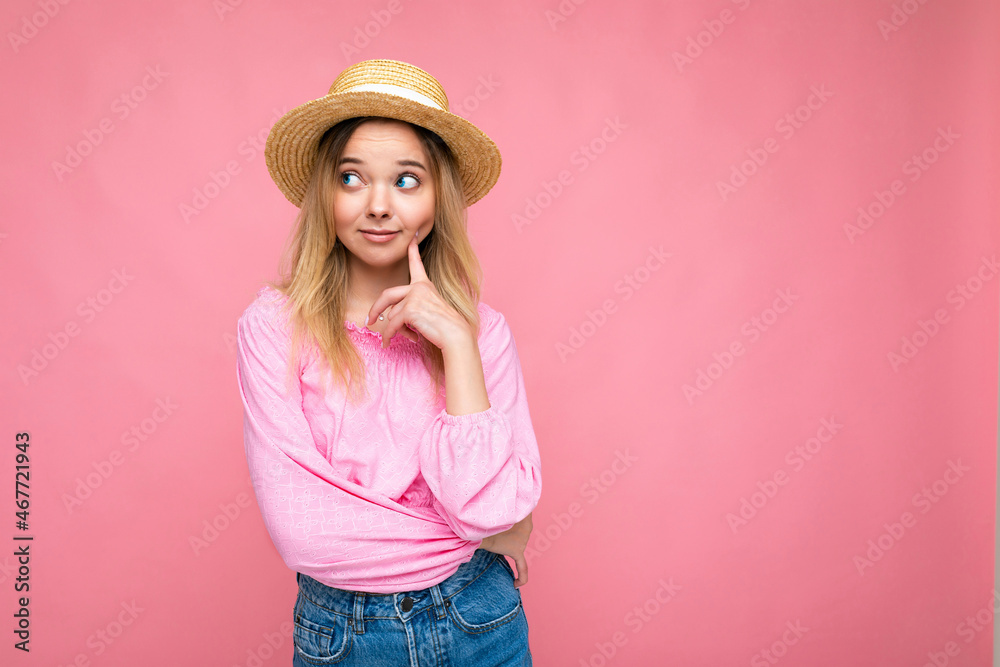 Photo shot of young beautiful cute thoughtful blonde woman wearing stylish pink crop top and straw hat isolated over pink background with copy space. Think concept Photo shot of young beautiful cute thoughtful blonde woman wearing stylish pink crop top and straw hat isolated over pink background with copy space. Think concept
