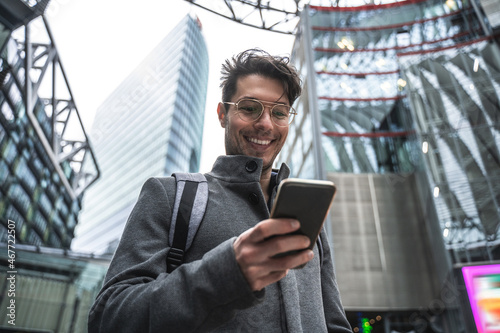 Male person wearing glasses using smartphone to sending message while standing