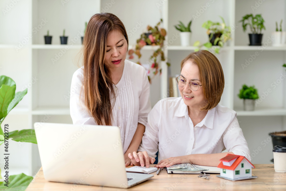 Two smiling middle-aged Asian business woman discussing using laptop computer in the office. Real estate agent or consultant. Two smiling middle-aged Asian business woman discussing using laptop computer in the office. Real estate agent or consultant.