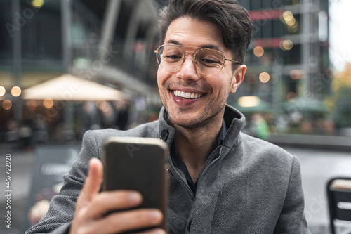 Man laughing out loud and chatting via video connection while sitting at street cafeteria