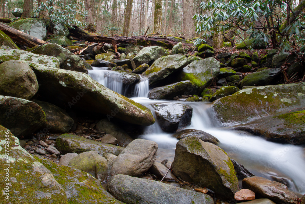 Ice cold, rapid moving fresh water from snow cap and glacial melt is rushing downstream, flowing through, around and cascading over mossy beds of large stones, to lower elevation, carrying sediment Ice cold, rapid moving fresh water from snow cap and glacial melt is rushing downstream, flowing through, around and cascading over mossy beds of large stones, to lower elevation, carrying sediment