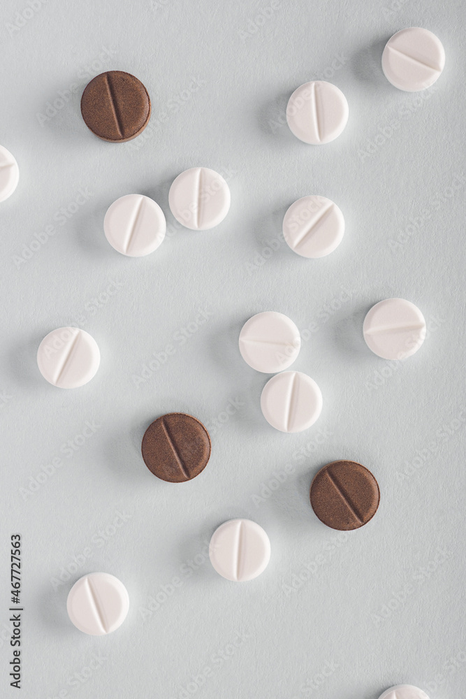 White and brown pills lie on a gray paper surface. Close-up. Light vertical background or illustration about medicine, health care, drugs, pharmacology. Tablets of different colors. Flat lay. Macro