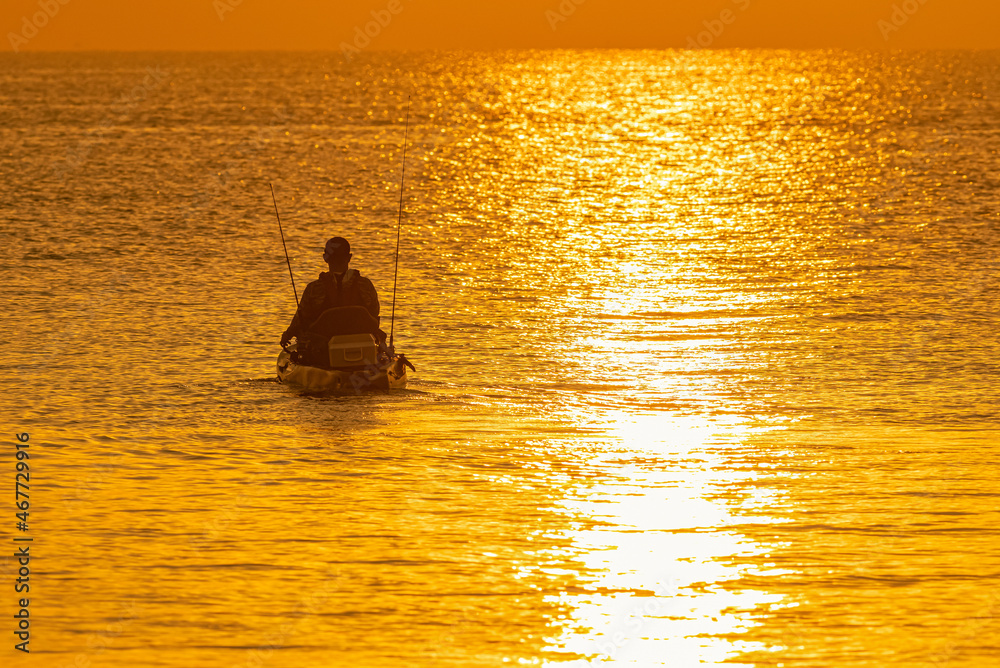 A man is fishing on a small boat in the bright morning light.
