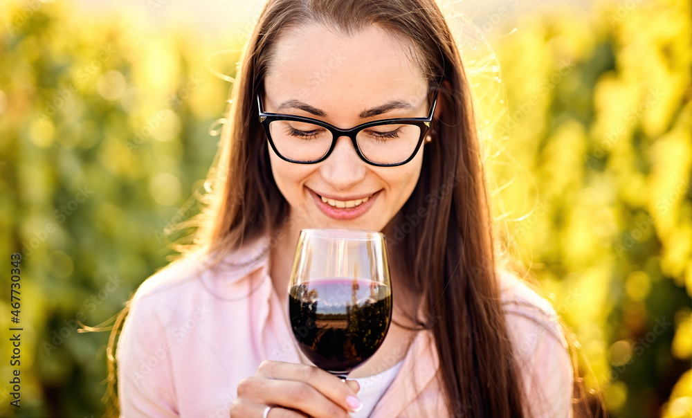 Portrait of a young, millennial woman holding and smelling a glass of organic bio red wine outdoors in a vineyard - Vine-growing, and wine-tasting concept Portrait of a young, millennial woman holding and smelling a glass of organic bio red wine outdoors in a vineyard - Vine-growing, and wine-tasting concept