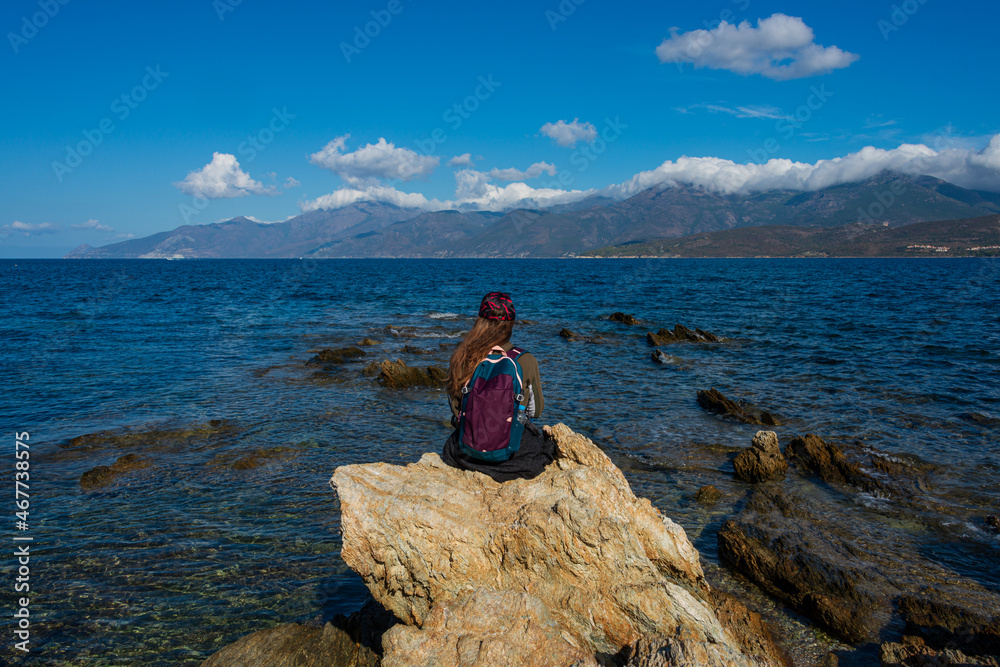 young female backpacker sitting on rocks alone beside the sea .Corsica France .