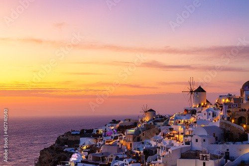 Greece vacation background. Famous iconic Oia village with traditional white houses and windmills during colorful sunset. Santorini island, Greece.