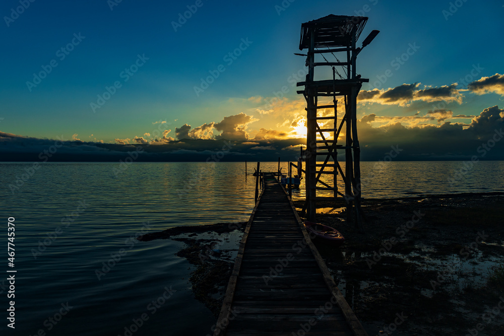 a slender watchtower by the pier on a deserted beach in the low season against the sunset