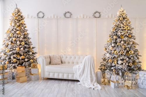 White living room interior with New Year trees decorated, gift boxes and modern sofa. Golden color
