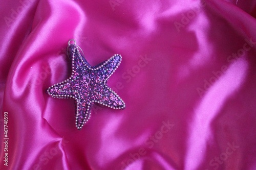 Bright pink satin background and lilac Christmas star toy. Silk fabric with pleats. Satin  silk or satin create a beautiful drapery. Fashionable design.