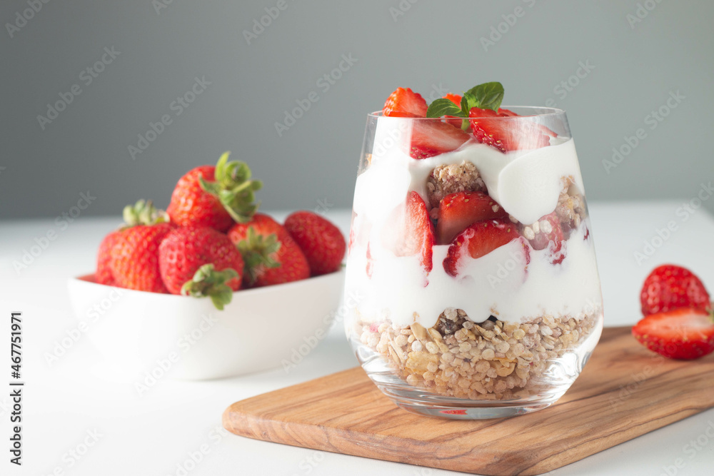 Glass with granola, yogurt and fresh strawberries on white table. Healthy breakfast bowl concept. Glass with granola, yogurt and fresh strawberries on white table. Healthy breakfast bowl concept.