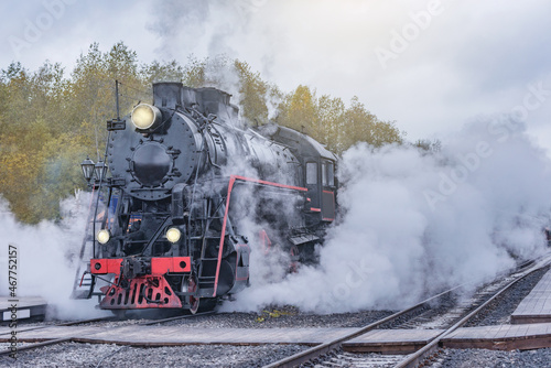 Retro steam train departs from the station wooden platform at cloudy evening.
