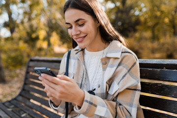 attractive young woman walking in autumn wearing jacket using phone