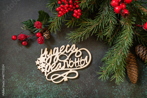 Holiday concept  merry Christmas card. Flat lay with fir tree branch and Christmas decorations with an inscription stating that miracles are real on a dark green stone background.