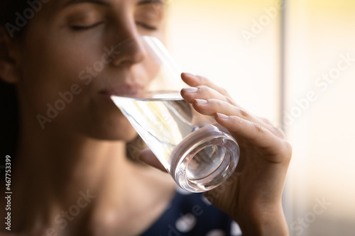 Pleasure in every sip. Close up shot of thirsty millennial hispanic woman with closed eyes drinking cool still purified clean water from glass. Young female hydrating relieving stress quenching thirst