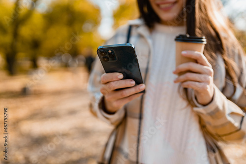 attractive young woman walking in autumn wearing jacket using phone