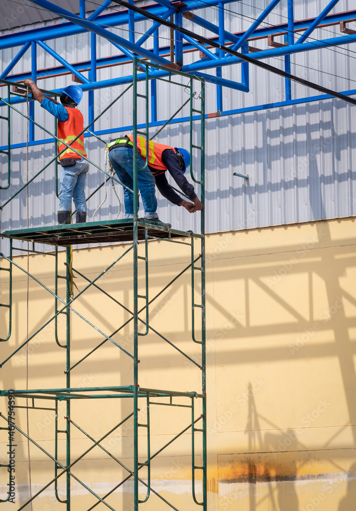 Two construction workers are installing high scaffolding for construction of warehouse building structure in construction site