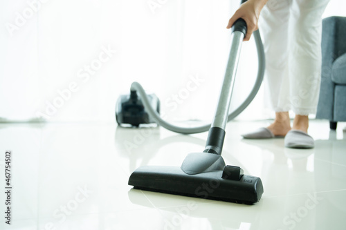 Asian young housekeeper using vacuum machine to clean a dirty floor in the living room.