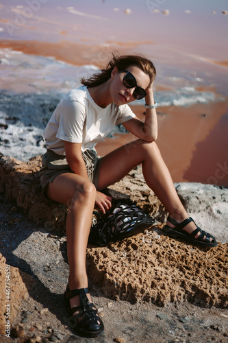 Beautiful, stunning and stylish young woman is sitting and posing on the rocks. Countryside landscape, nature, water and stones at the background. Summertime, summer, outdoor, lifestyle 
