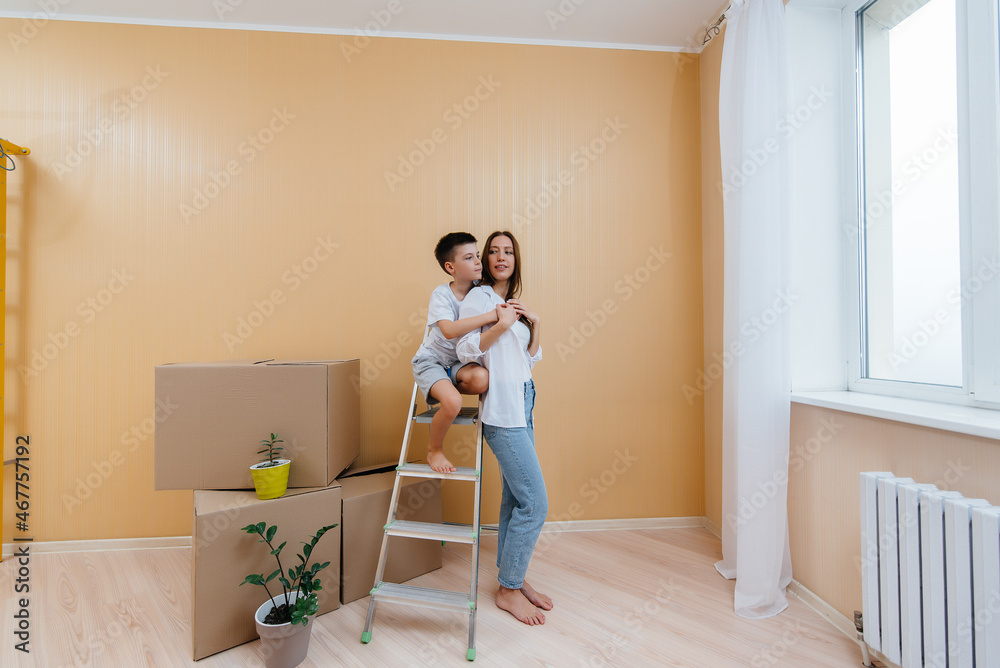 A young woman and her son are standing in front of the boxes and enjoying the housewarming after moving in. Housewarming, delivery and freight transportation, purchase of real estate.