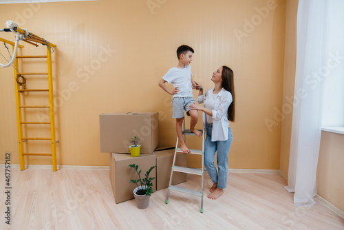 A young woman and her son are standing in front of the boxes and enjoying the housewarming after moving in. Housewarming, delivery and freight transportation, purchase of real estate. © Andrii