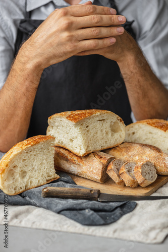 an adult European male baker holds a round fresh bread in his hands. a man in a bakery holds a yeast-free bread on sourdough and a baguette. cool and healthy bread for the whole family. vegan food for