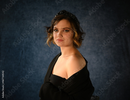 Portrait of a young girl on a dark background in a beautiful dress and a headdress made of precious stones