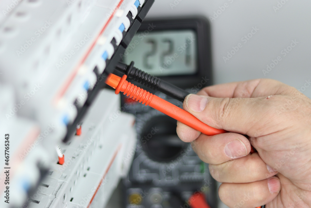 An electrical engineer measures the parameters of electrical circuits with a multimeter in an electrical panel for process control.