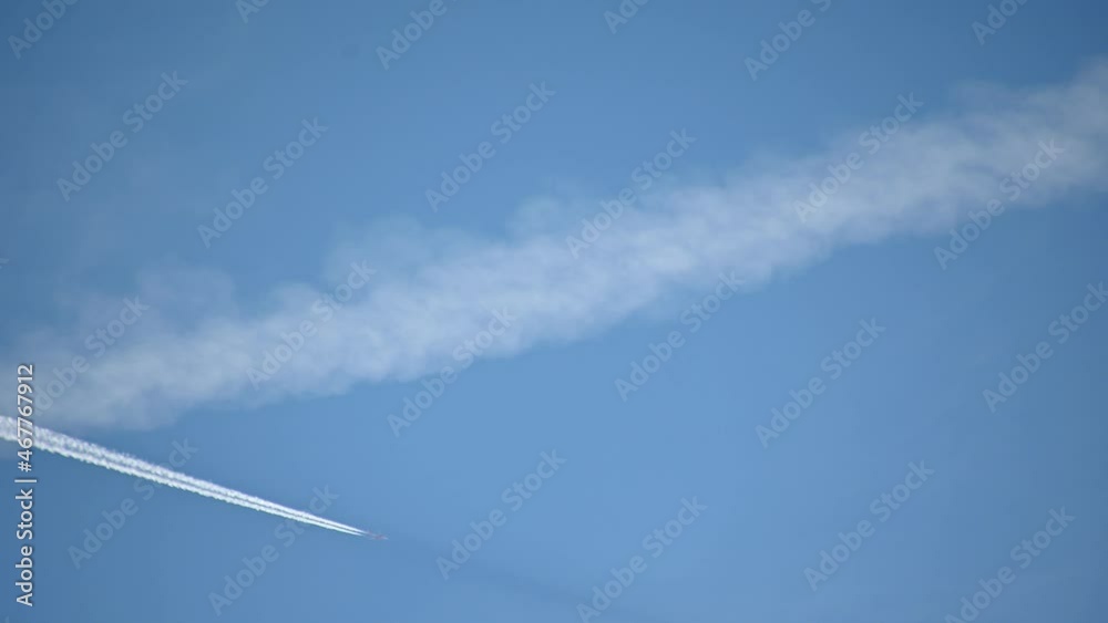 High flying airplane jet leaves a contrail. Plane fly against blue sky leaving water vapor contrails behind as seen from the ground. Aircraft passing by. Real time, static shot High flying airplane jet leaves a contrail. Plane fly against blue sky leaving water vapor contrails behind as seen from the ground. Aircraft passing by. Real time, static shot
