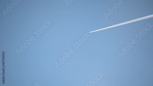 High flying airplane jet leaves a contrail. Plane fly against blue cloudless sky leaving water vapor contrails behind as seen from the ground. Aircraft passing by. Real time, static shot