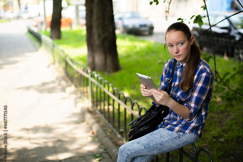 A teen girl sits with a tablet in an alley A teen girl sits with a tablet in an alley