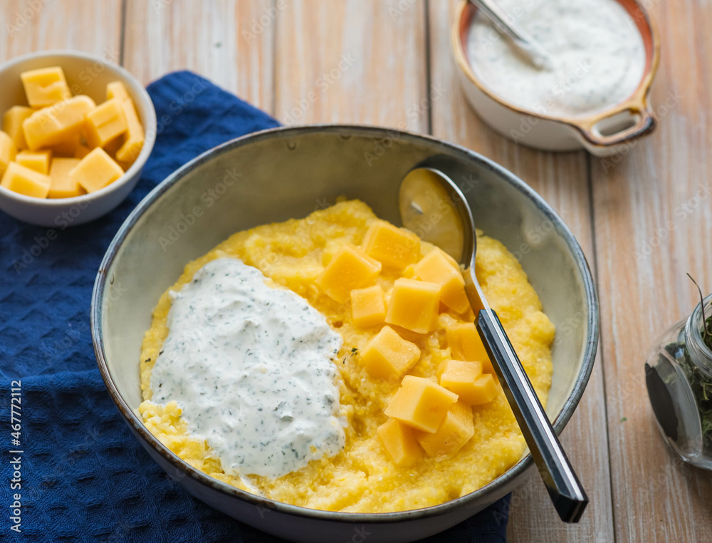 Corn porridge with cheese and sour cream sauce in a gray plate on a wooden background. Georgian cuisine. Corn porridge with cheese and sour cream sauce in a gray plate on a wooden background. Georgian cuisine.
