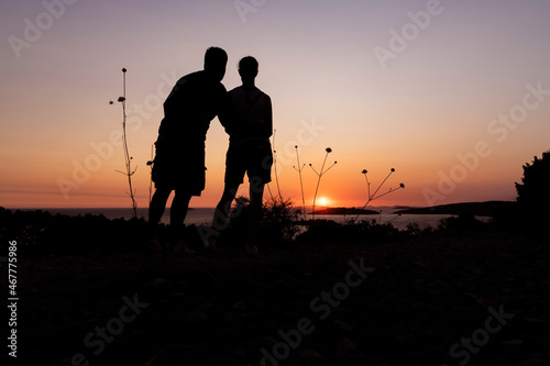 Silhouette of man and woman watching summer sunset on the horizon at the croatian coast of Rogoznica, from the hill above the sea