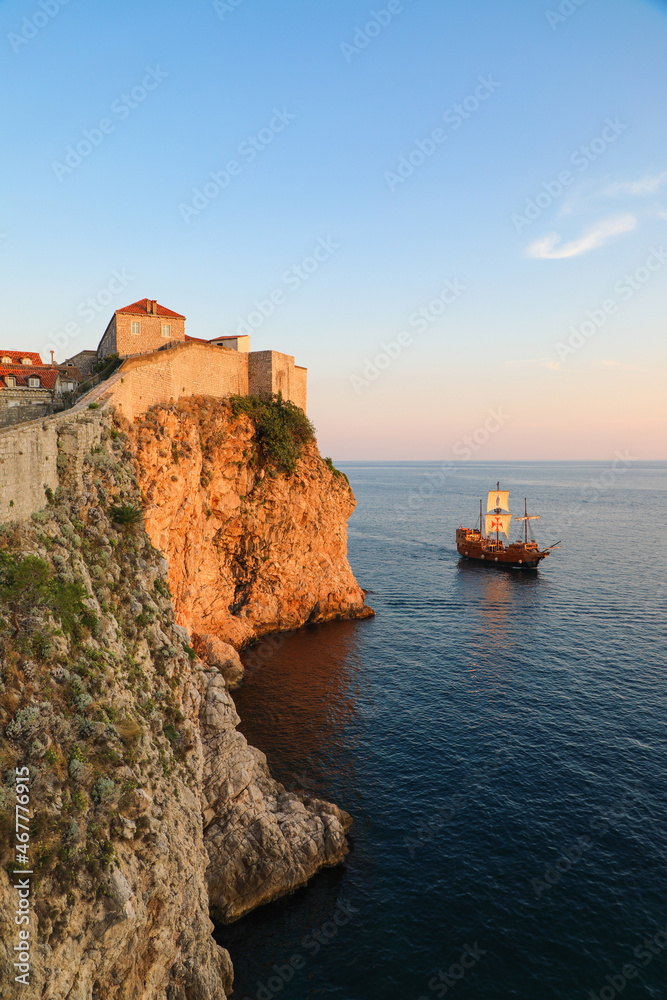 Fortress walls of Dubrovnik with a pirate galleon ship sailing in the harbor at sunset