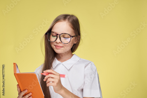 schoolgirl with textbook in hands learning childhood yellow background