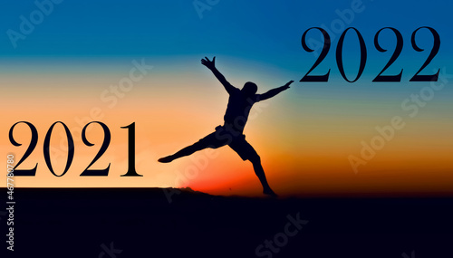  Silhouette of a young man jumping between 2021 and 2022 against the backdrop of a sunset. happy new year 2022.