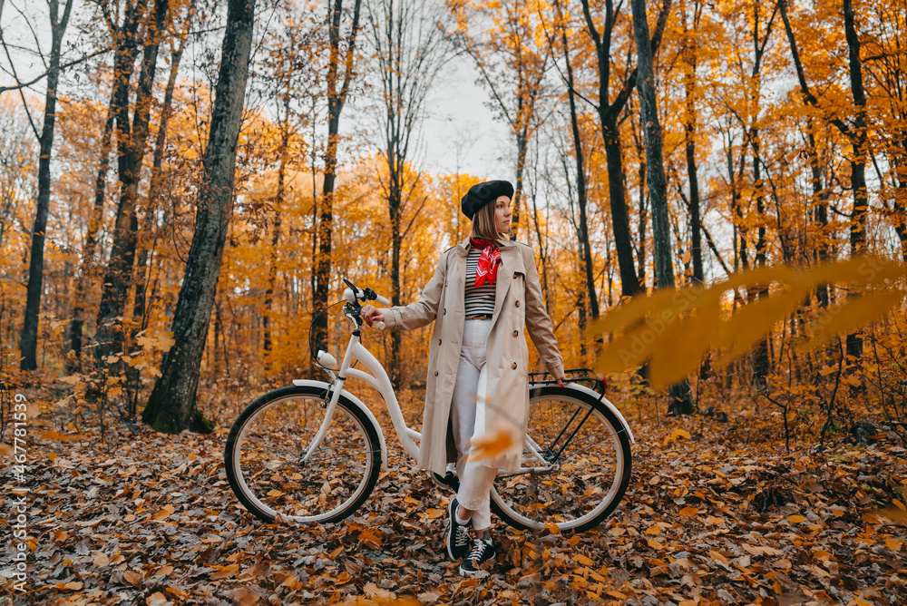 Obraz premium Young woman in classic trench coat with retro bicycle in yellow autumn park. Amazing scene of trendy girl on nature background. Environmentally friendly mode of transport