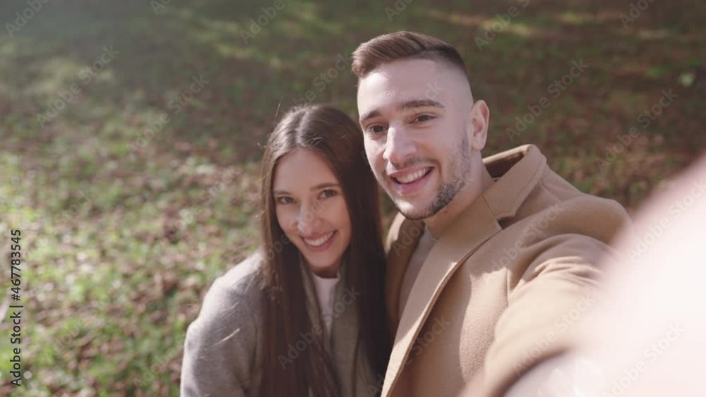 Slow motion – Young caucasian couple in coats smiling and doing a selfie in a park on a sunny day in autumn Slow motion – Young caucasian couple in coats smiling and doing a selfie in a park on a sunny day in autumn