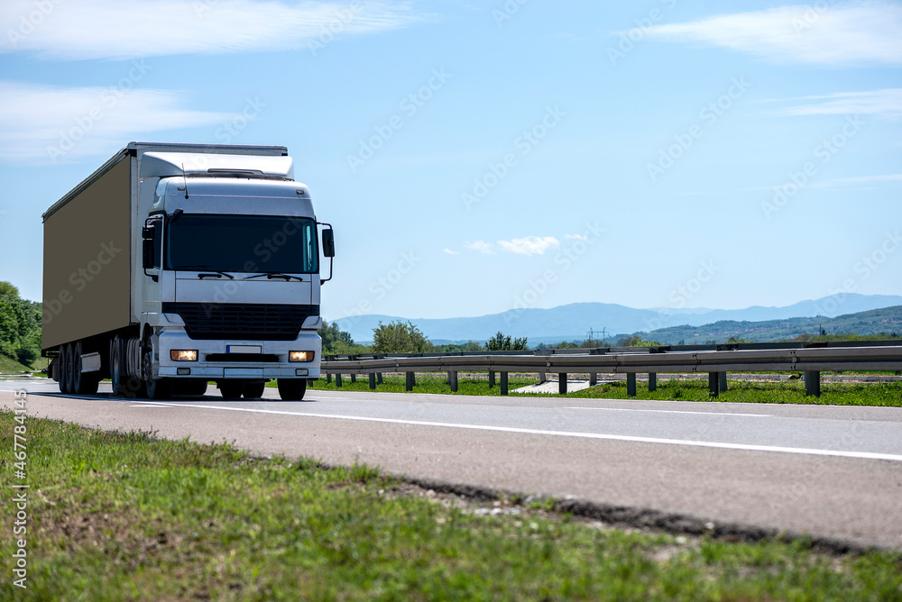 White truck driving on asphalt road in a rural landscape.